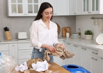 A woman carefully practicing trash sorting in a Tokyo apartment kitchen, separating bottles and paper into labeled bins