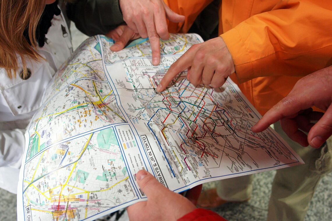 Group of people examining a detailed map, with fingers pointing to a location.