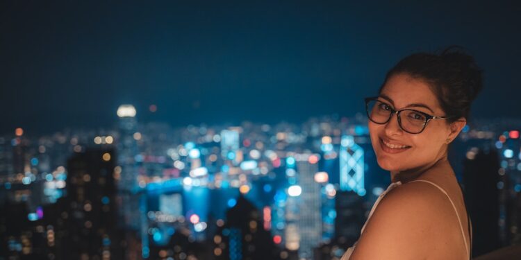a-woman-in-a-rooftop-bar-night-unsplash - TOKYOwebzine A woman holding a cocktail glass at one of Tokyo's rooftop bars, with the glowing city skyline visible behind her at dusk.