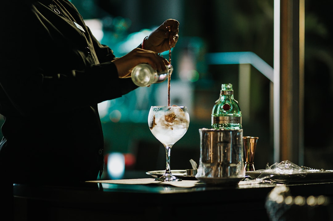 Ein Barkeeper gießt sorgfältig einen Signature-Cocktail in einer Tokioer Dachbar aus, die Lichter der Stadt spiegeln sich im Glas.
