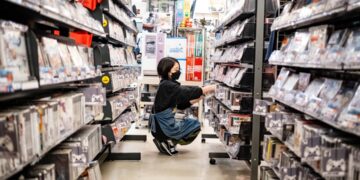 convenience-store-worker-stocking-shelves-japan-unsplash - TOKYOwebzine A konbini culture worker restocking fresh food shelves inside a brightly lit Tokyo convenience store at night