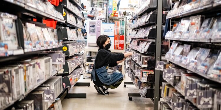A konbini culture worker restocking fresh food shelves inside a brightly lit Tokyo convenience store at night