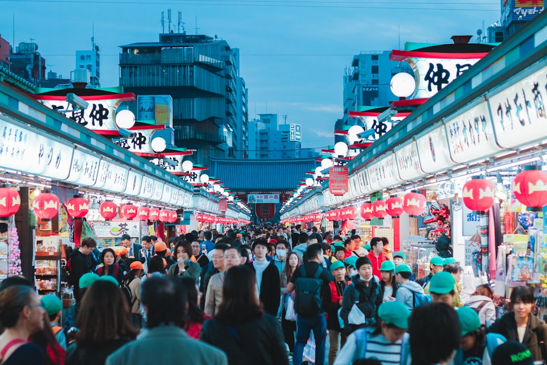 A diverse group of people browse stalls at outdoor food festivals in a Tokyo park surrounded by green trees.