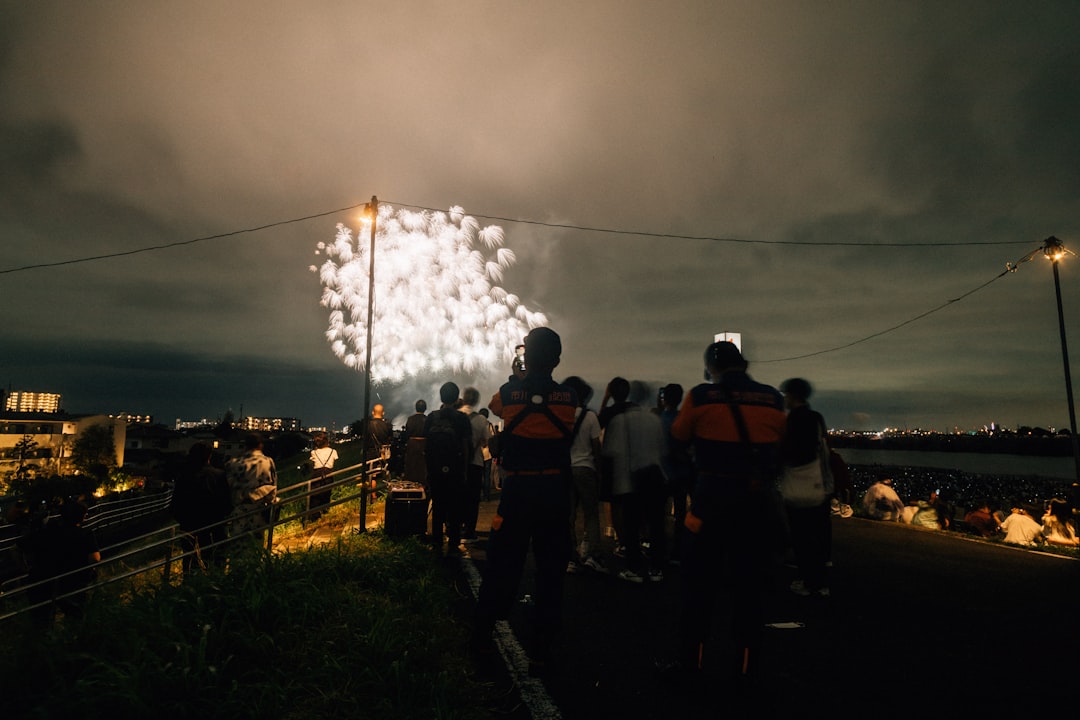 A group of friends sit on a picnic mat and look up at the Hanabi Tokyo fireworks display lighting the dark summer sky.