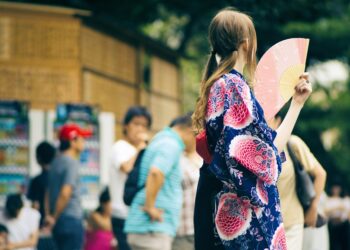 A woman in Tokyo uses a traditional folding fan to stay cool on a hot summer day, a simple ritual that works beautifully.