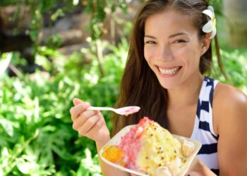 A woman savors a bowl of kakigori at aTokyo shop, holding a small spoon over a mountain of shaved ice with fresh fruit syrup.