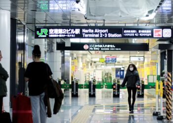 A traveller reviews their boarding pass at a Tokyo airport departure gate, aware of the departure tax added to their ticket.