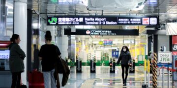 A traveller reviews their boarding pass at a Tokyo airport departure gate, aware of the departure tax added to their ticket.