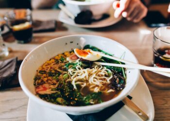woman-eating-ramen-tokyo-restaurant-unsplash - TOKYOwebzine A woman enjoying a bowl of gluten-free ramen at a Tokyo noodle restaurant, smiling over her wheat-free meal.