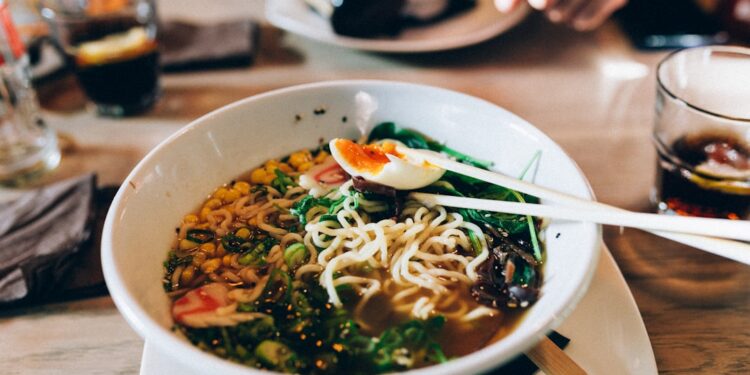 woman-eating-ramen-tokyo-restaurant-unsplash - TOKYOwebzine A woman enjoying a bowl of gluten-free ramen at a Tokyo noodle restaurant, smiling over her wheat-free meal.