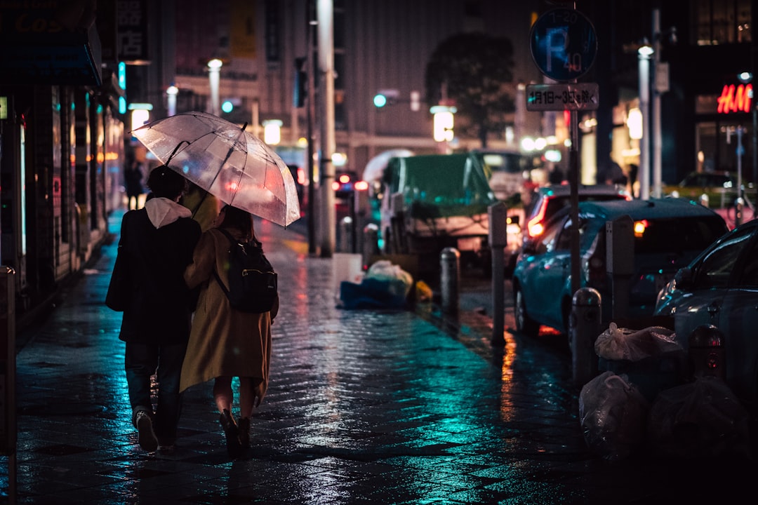 A woman walks a Tokyo street holding a stylish umbrella during rainy season, dressed in light breathable clothing