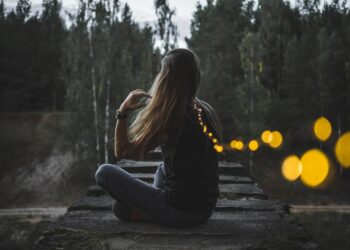 A woman stands quietly beside the River during a Fussa firefly viewing evening, watching soft lights reflect on the water
