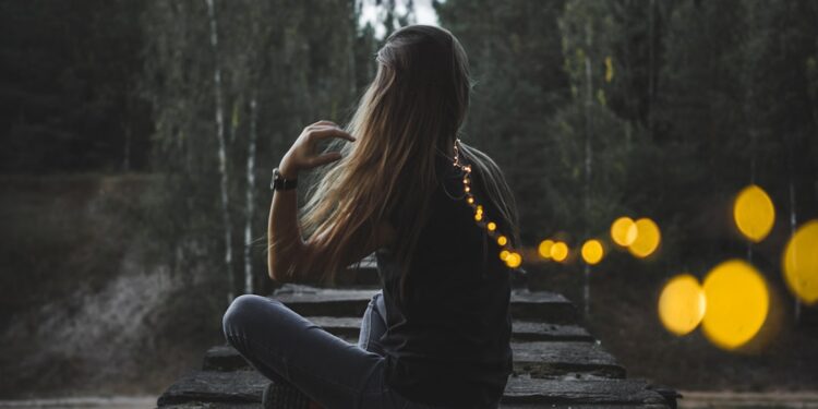 A woman stands quietly beside the River during a Fussa firefly viewing evening, watching soft lights reflect on the water