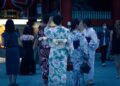 A woman in a yukata smiles while watching the Hanabi Tokyo fireworks show at night, surrounded by a crowd of festival-goers.