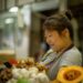 asian-woman-grocery-shopping-unsplash - TOKYOwebzine A shopper carefully selecting fresh sashimi trays at a Tokyo depachika basement food hall