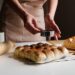 baker-slicing-japanese-milk-bread-loaf-unsplash - TOKYOwebzine A baker slices a thick loaf of milk bread in a Tokyo bakery, showing its soft and pillowy crumb