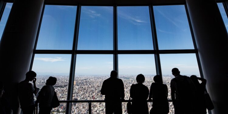 business-presentation-meeting-tokyo-unsplash - TOKYOwebzine A business executive reviews documents at a Tokyo headquarters office, with a city skyline visible through the window.