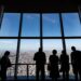 A business executive reviews documents at a Tokyo headquarters office, with a city skyline visible through the window.