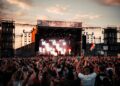 A performer on stage at Tokyo Idol Festival with a large crowd of fans cheering in the Odaiba waterfront venue