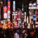 tokyo-street-fashion-unsplash - TOKYOwebzine A crowded neon-lit street in Japan at night, with colorful signs and storefronts lining the sidewalk as shoppers pass by.