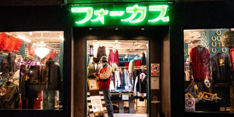 vintage-linen-clothes-tokyo-shop-unsplash - TOKYOwebzine A woman carefully examines natural fibre garments in a Tokyo secondhand wardrobe shop