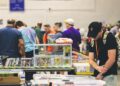 A visitor carefully browsing doujinshi at a Comic Market circle table inside Tokyo Big Sight