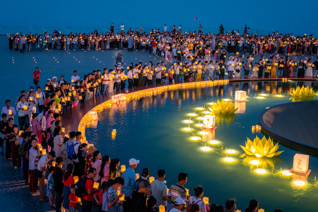 A group of people release glowing floating lanterns on a Tokyo river as part of Obon season farewell rituals at dusk.