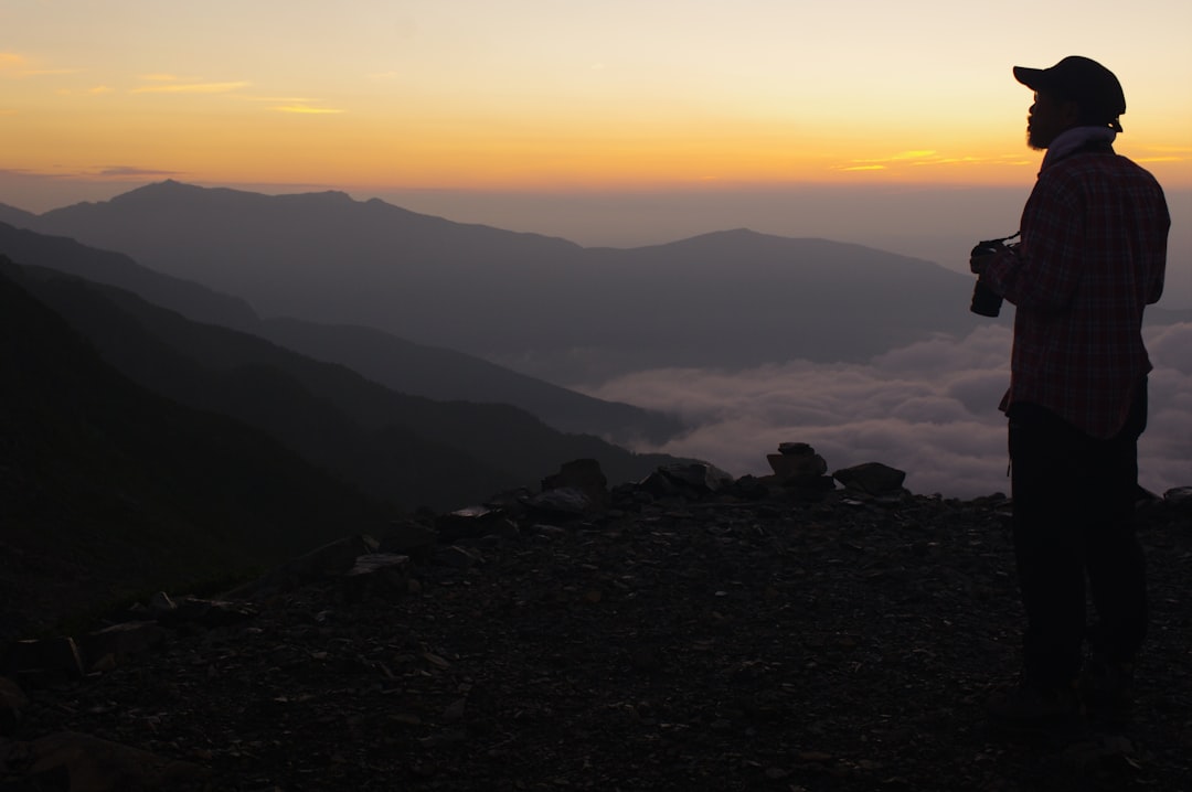 A solo climber watches the goraikō sunrise from the upper trail during Mt Fuji climbing season, wrapped in a thermal jacket.