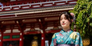 woman-in-yukata-ryokan-dinner-unsplash - TOKYOwebzine A guest in a yukata robe sits before a Tokyo ryokan kaiseki dinner table set with seasonal dishes and paper lanterns.