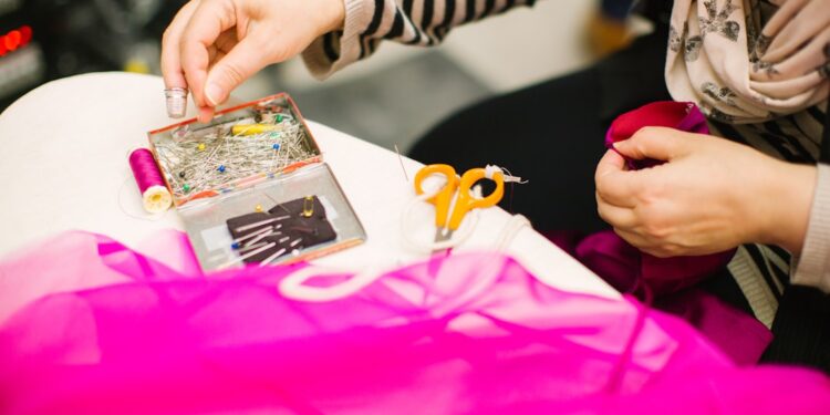 woman-sewing-clothes-repair-workshop-unsplash - TOKYOwebzine A volunteer helps a woman mend a jacket at a repair café in Tokyo, showing community mending in action.