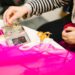 woman-sewing-clothes-repair-workshop-unsplash - TOKYOwebzine A volunteer helps a woman mend a jacket at a repair café in Tokyo, showing community mending in action.
