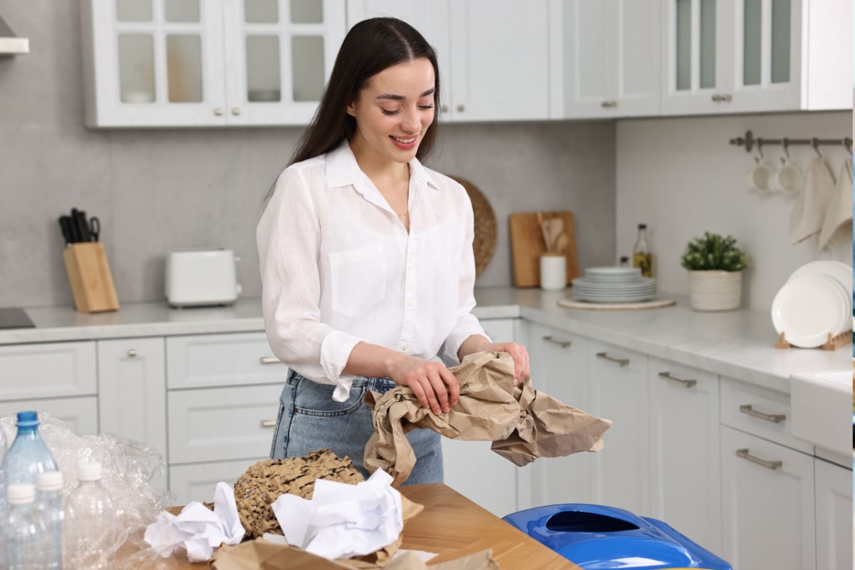 Una mujer practicando cuidadosamente la clasificación de basura en la cocina de un apartamento de Tokio, separando botellas y papel en contenedores etiquetados