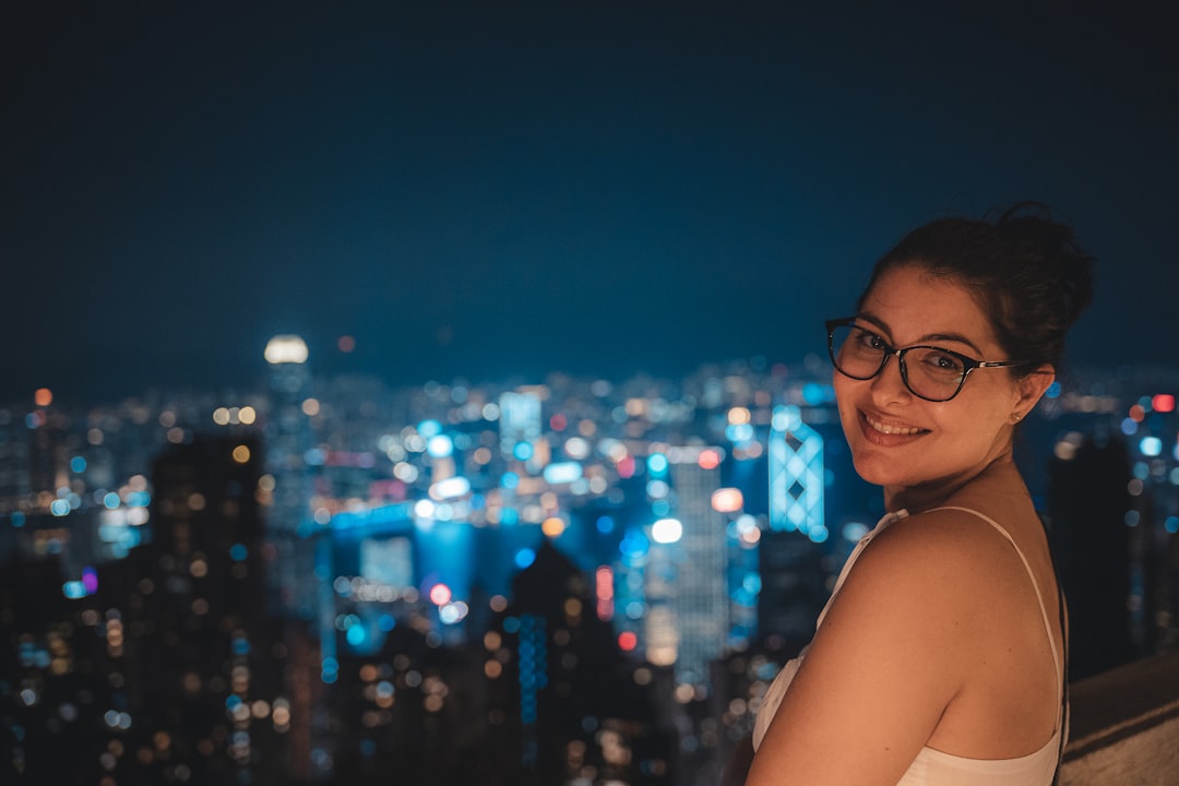 A woman holding a cocktail glass at one of Tokyo's rooftop bars, with the glowing city skyline visible behind her at dusk.