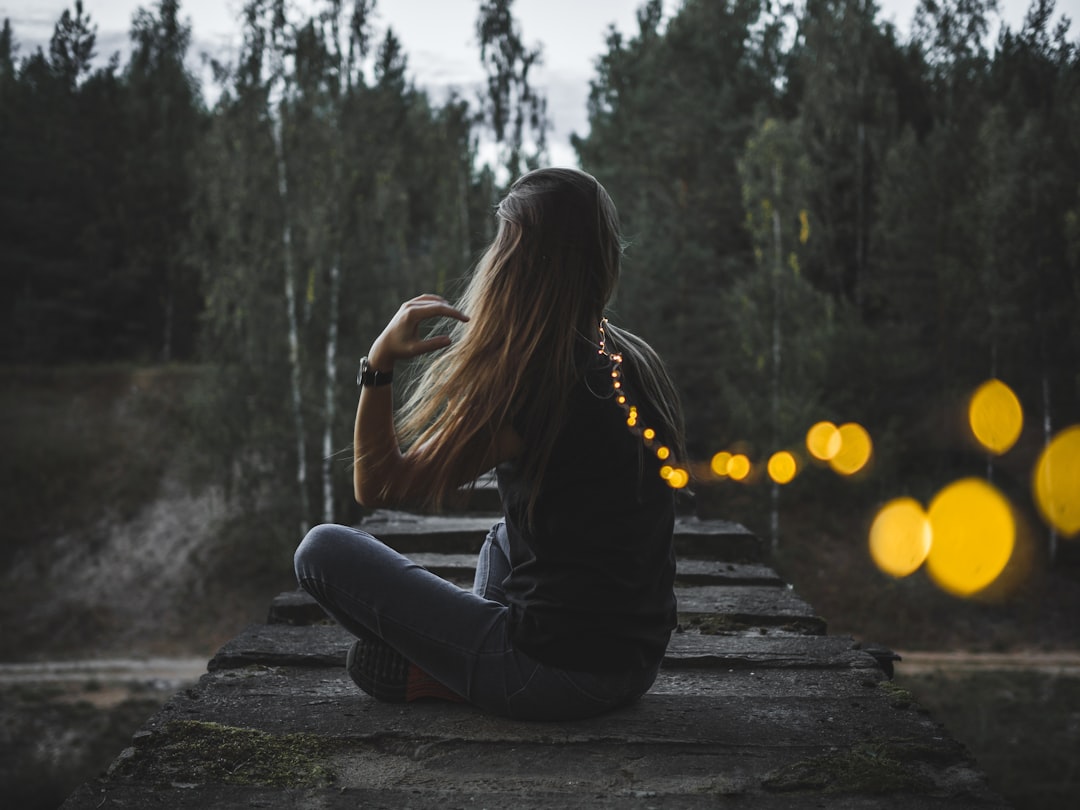 Una donna che sta tranquillamente accanto al fiume durante una serata di osservazione delle lucciole a Fussa, guardando le luci soffuse riflettersi sull'acqua.