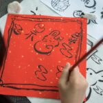 A young child concentrates on a brush painting activity during summer kids workshops in Tokyo, surrounded by mineral pigments